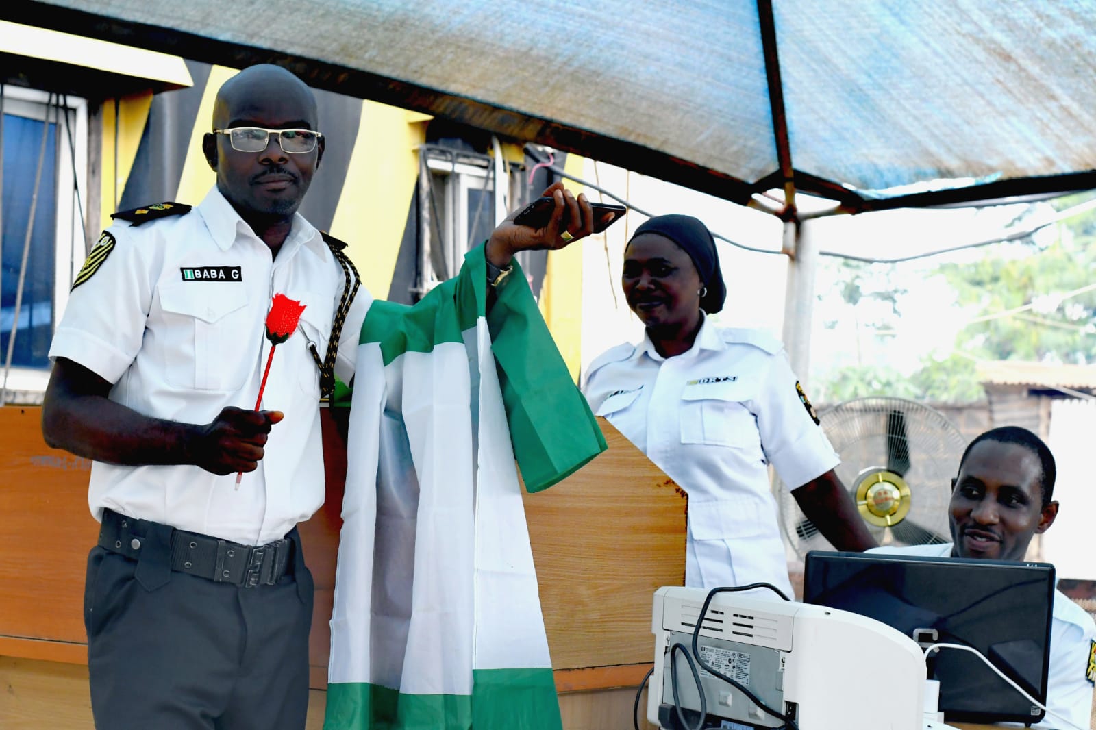 Uniformed officers holding a Nigerian flag and a red rose