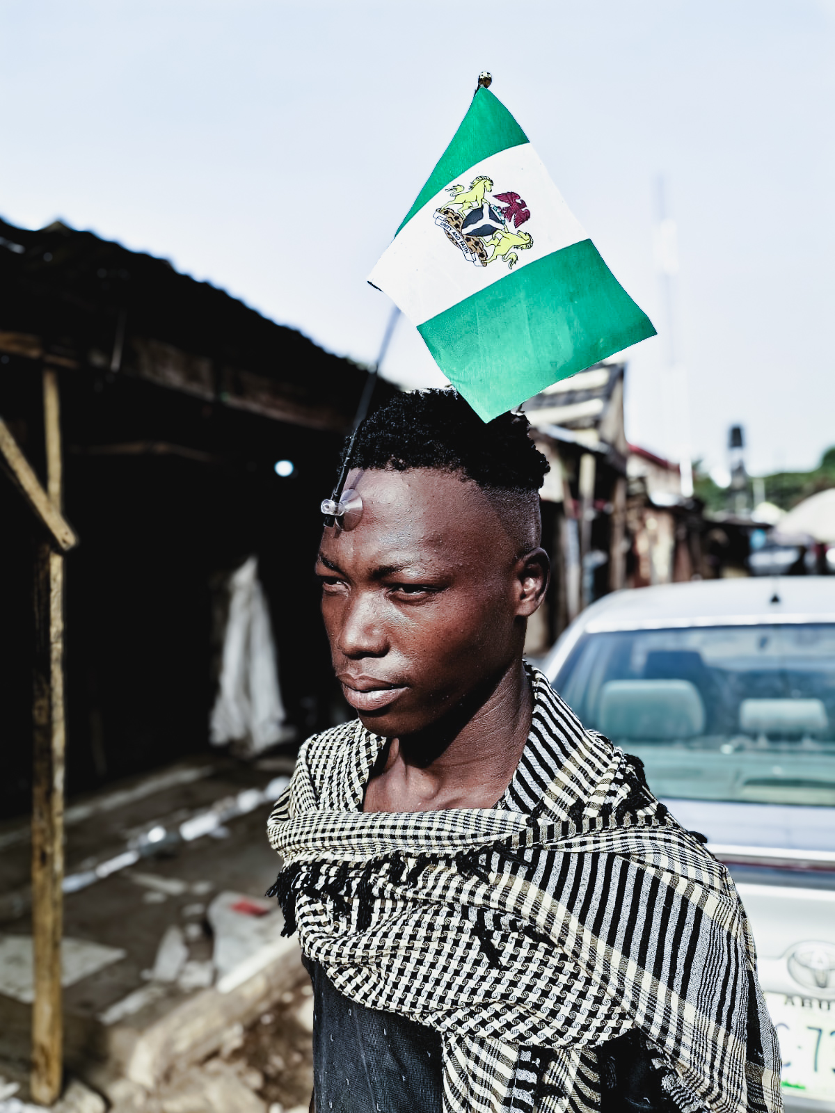 A young man in a Nigerian street with the coat-of-arms flag above his head