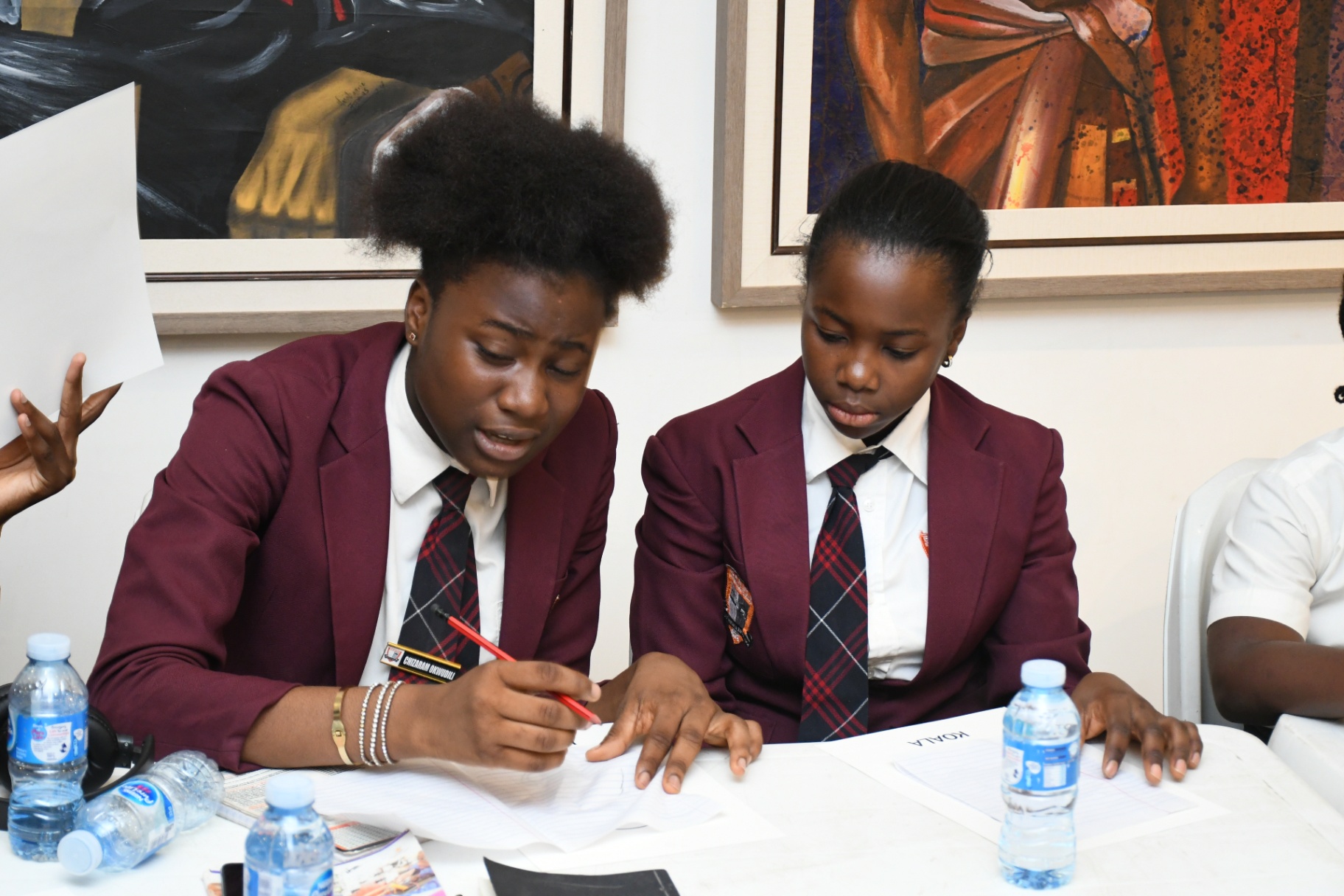 Two secondary school girls in maroon blazers concentrating over a shared drawing