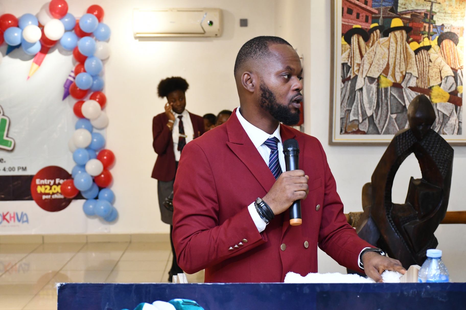 A man in a burgundy blazer speaking into a microphone at the Children's Day festival