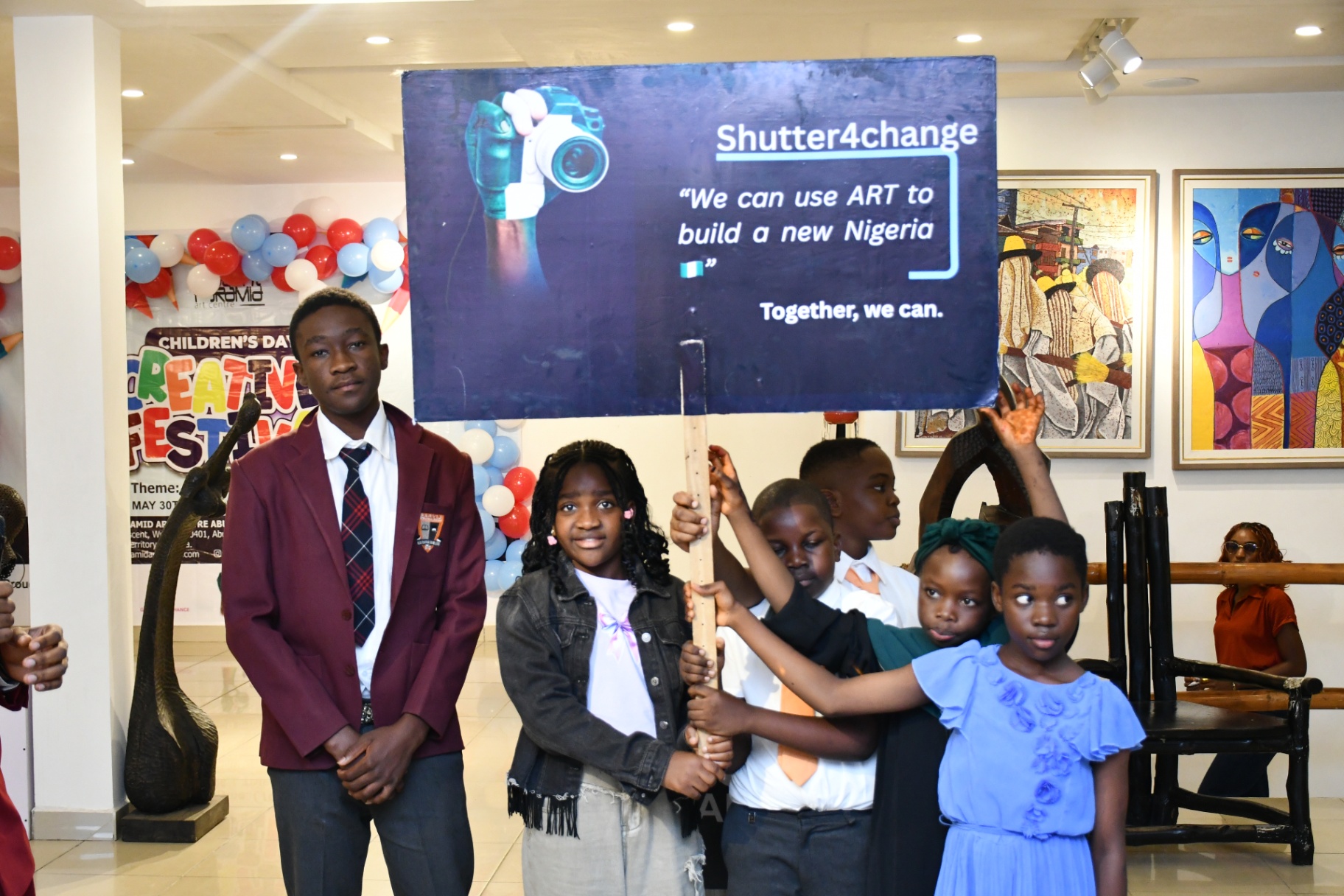 A boy in a maroon blazer holding the Shutter4change placard while classmates gather around